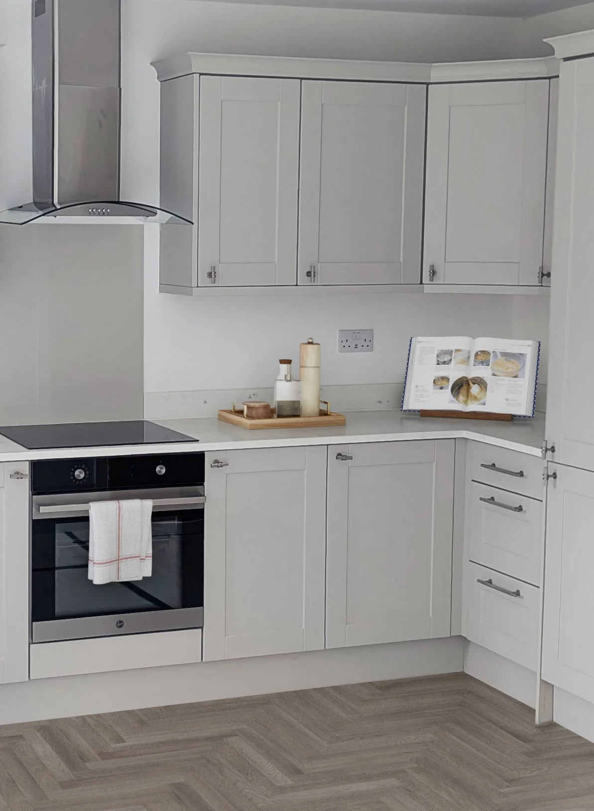 Kitchen with white cabinets, countertop, oven with towel, open cookbook, and small tray with condiments.