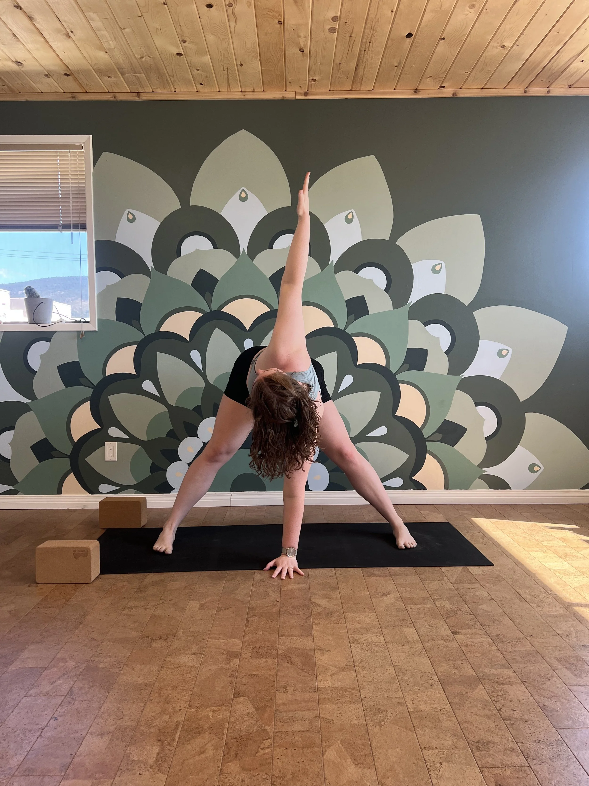 A person doing a yoga pose in front of a large, stylized flower mural on the wall.