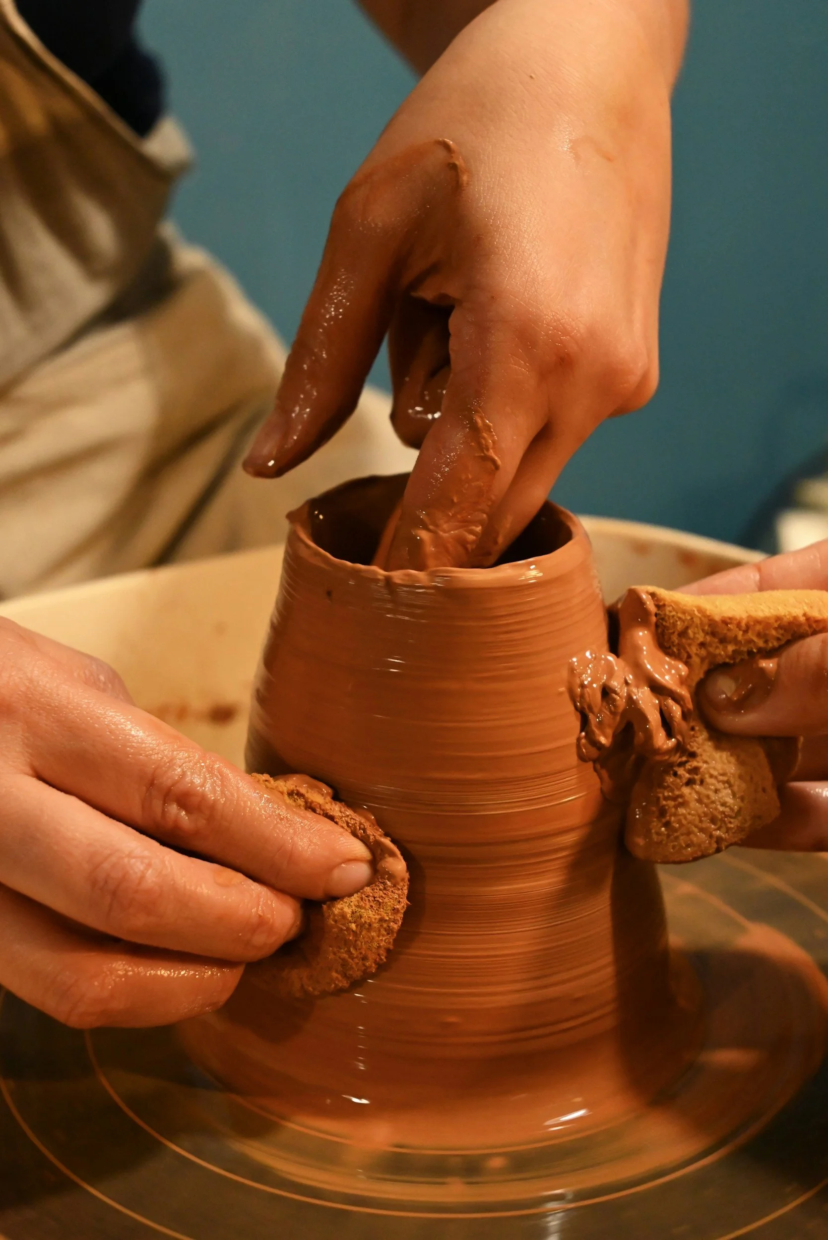 Close-up of hands shaping a clay pot on a pottery wheel, with wet clay and tools in use.
