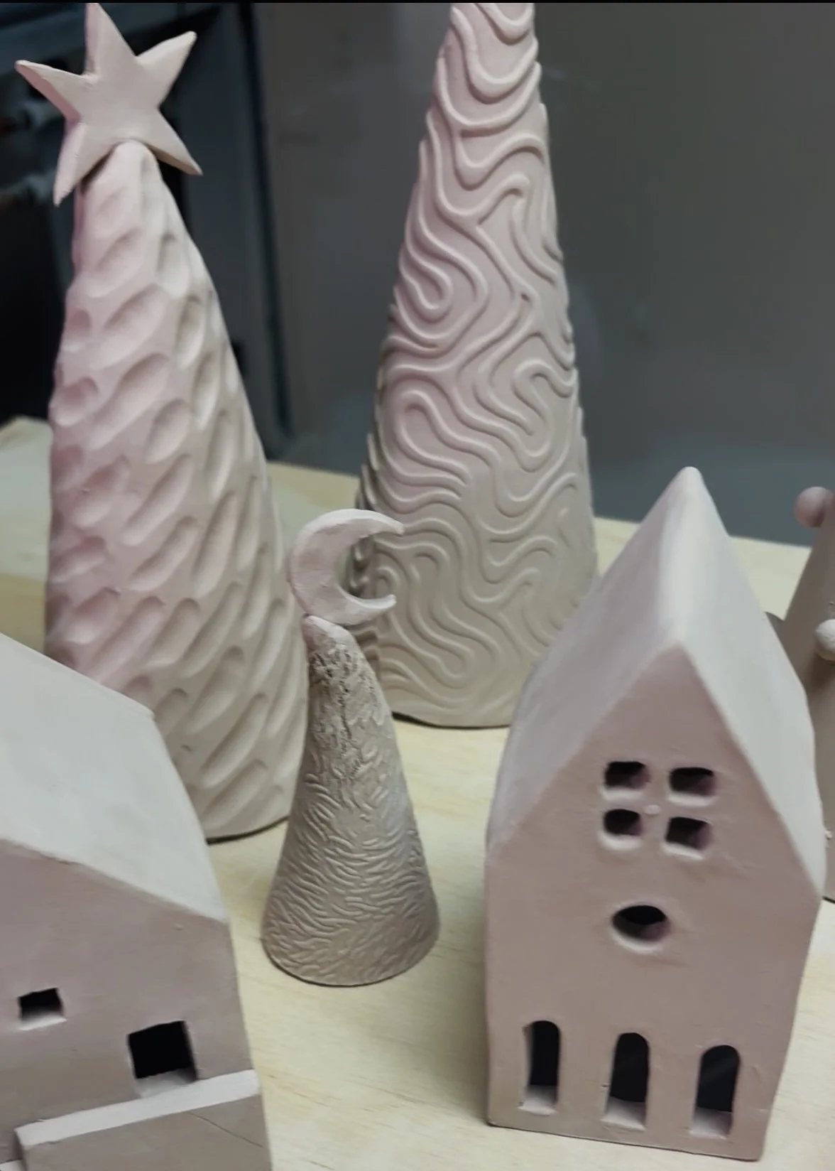 Collection of ceramic holiday decorations, including Christmas trees, a house, and other shapes, some with textured or carved designs.