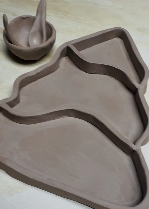Unfinished tree charcuterie plate, small bowl with two spoons beside it on a light wooden surface.