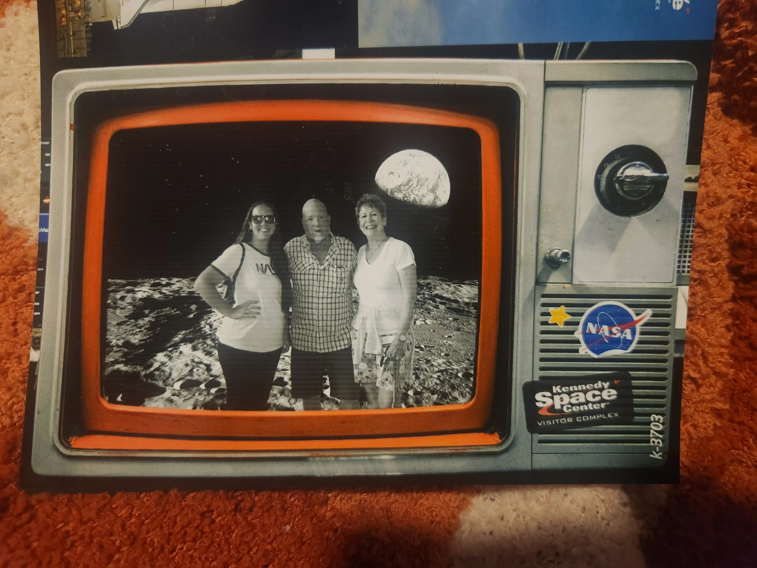 A vintage style photo frame with NASA and Kennedy Space Center logos, featuring two women and one man smiling on the lunar surface with Earth visible in the distance.