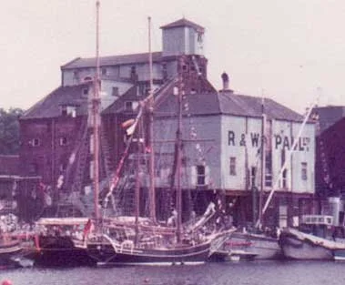 A historic harbor scene with boats docked and a large industrial building labeled R & W PACE in the background.