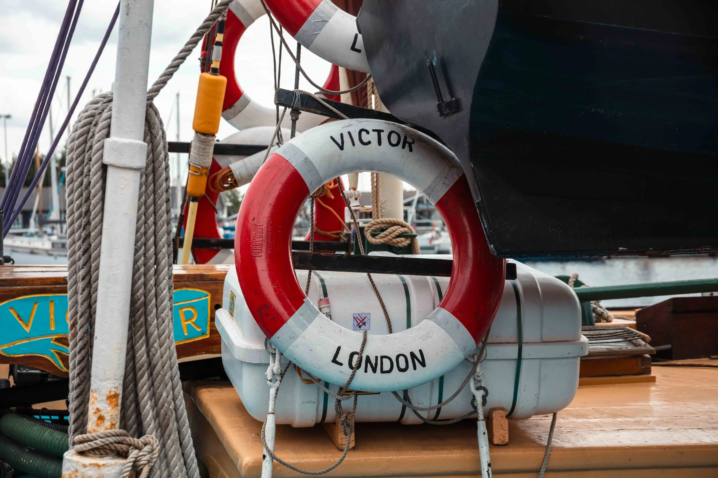 Close-up of a boat dock with life rings attached, one bearing the words 'Victor London,' surrounded by ropes and other nautical equipment.