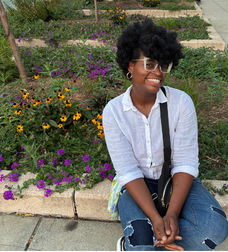 B.E.E A Liberator President Keiarah posing shyly beside a flower bed.