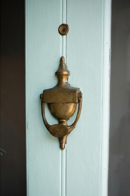 A vintage brass door knocker mounted on a light blue wooden door.