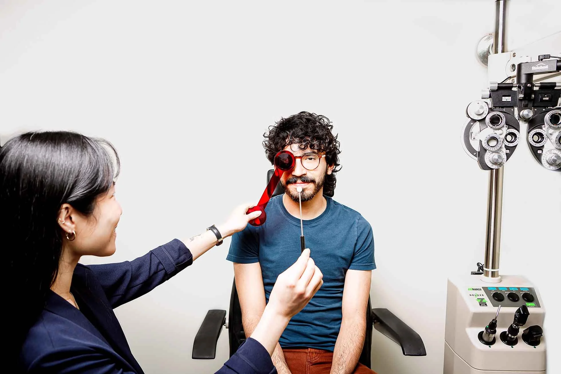 A doctor conducts eye tests on a young man using specialized ophthalmic equipment in a medical office.