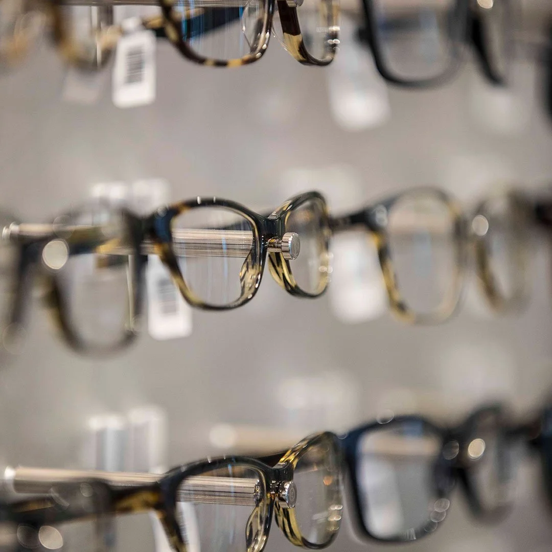 Multiple pairs of eyeglasses displayed on a store rack, with some pairs having a tortoiseshell pattern and others being black.