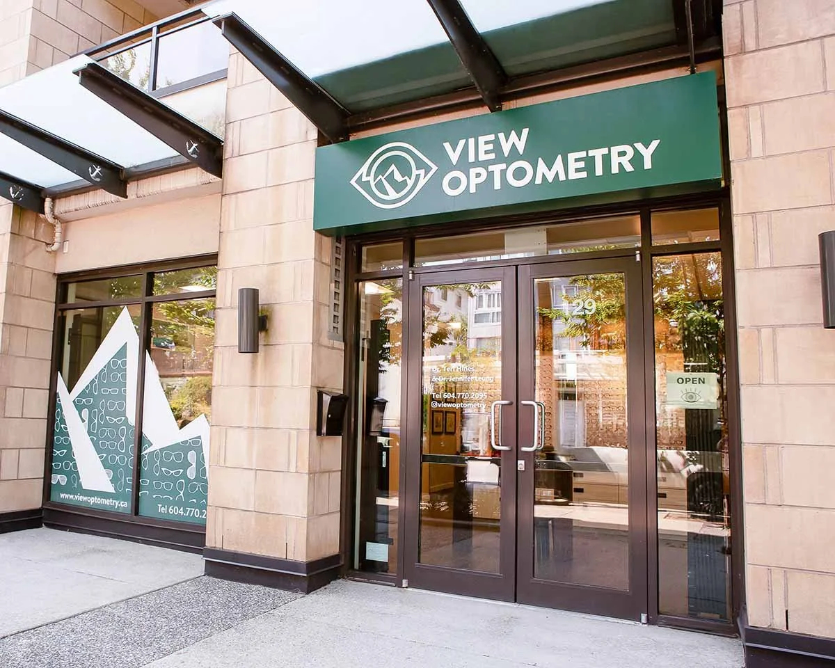 Entrance to View Optometry with glass doors, a green sign with a logo and text, and large window displays.