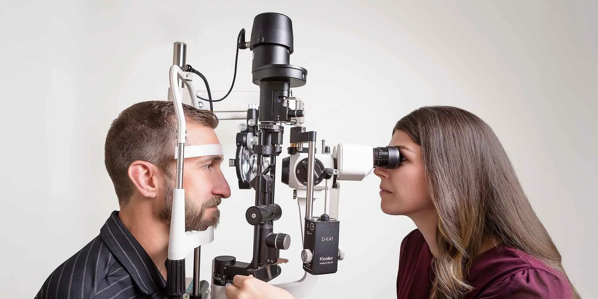 An eye doctor examining a man's eyes using a slit lamp in an optometry clinic.