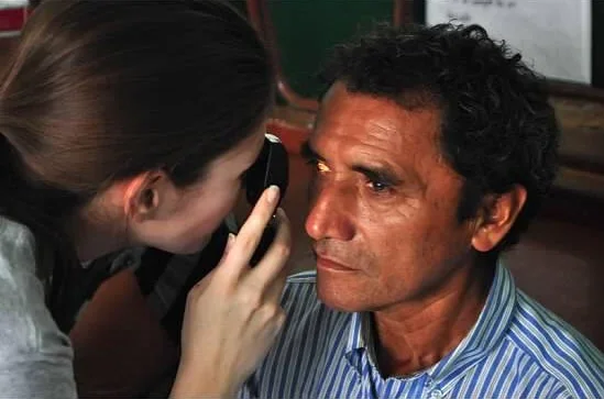 A woman using a flashlight to look closely at a man’s eye.