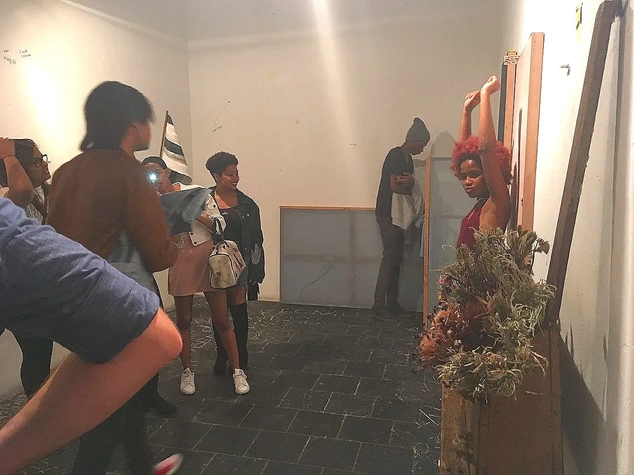 Een groep mensen kijkt naar een standbeeld van een vrouw met Rode haar. De vrouw met het beeld staat met haar armen omhoog en houdt één arm gebogen boven haar hoofd en de andere arm recht omhoog.