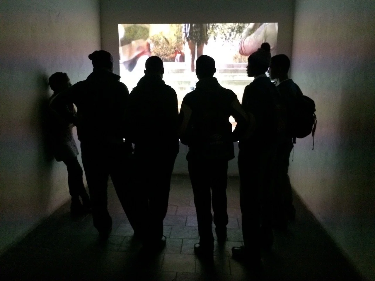 Groep mensen kijkt naar een filmpje op een muur in een donker interieur.
