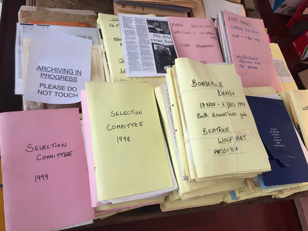 Een tafel vol met gestapelde documenten en mappen in verschillende kleuren, met etiketten en aantekeningen.