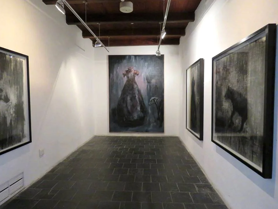 Een kunstgalerie met vier schilderijen, inclusief een grote centrale doek van een dier dat lijkt op een hond of wolf, in een donkere stijl.