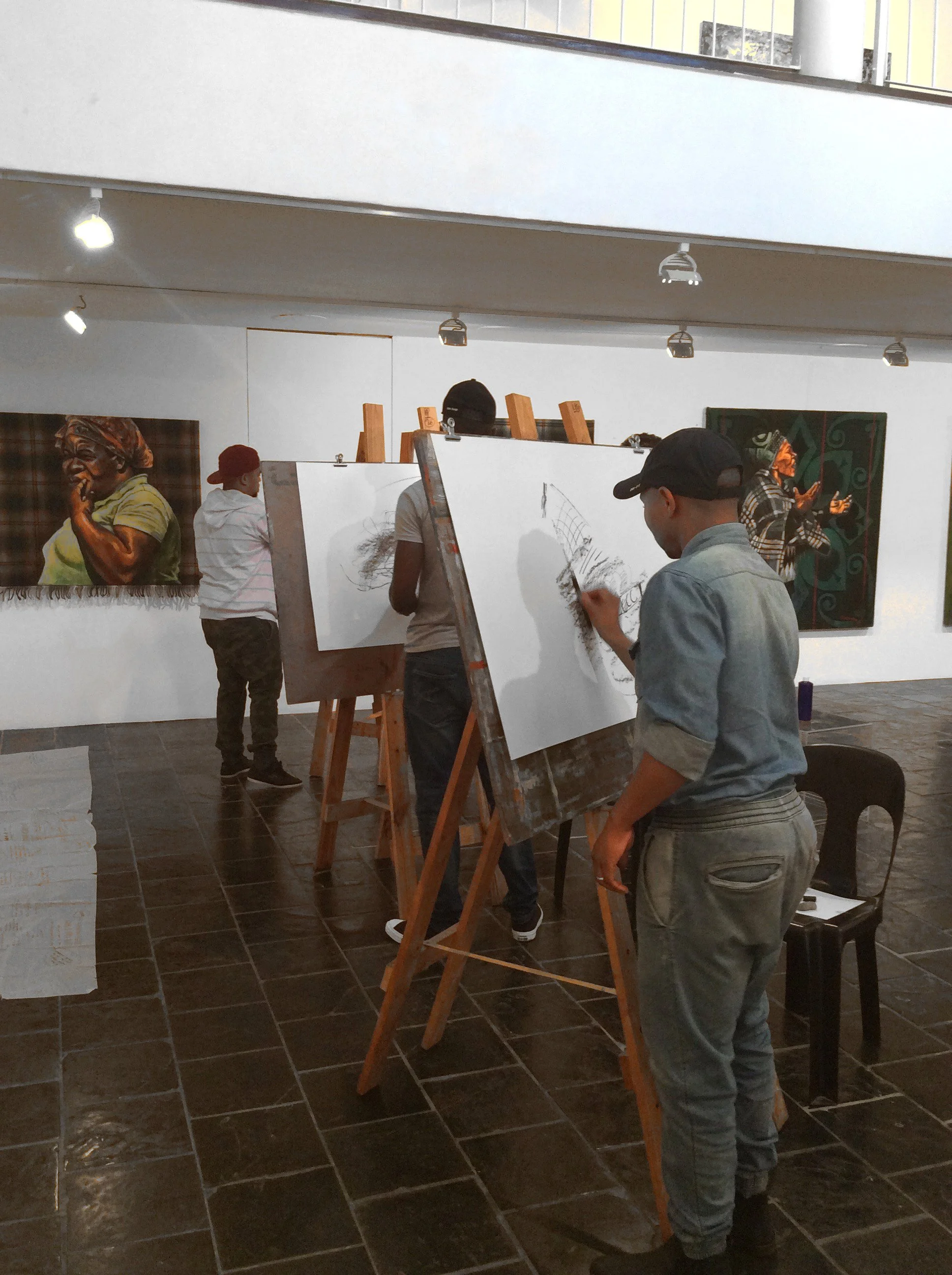 Mensen die in een kunstgallery staan en tekenen op een wit doek, met schilderijen aan de muur op de achtergrond.