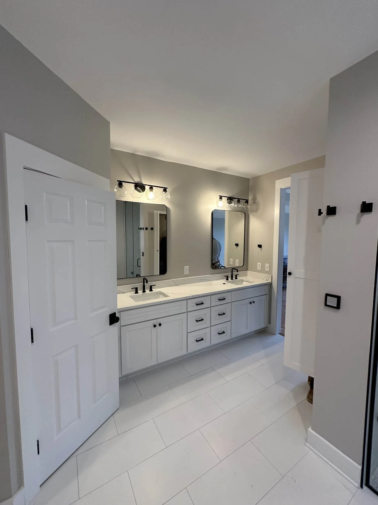 Primary bathroom remodel with double vanity, white cabinetry, black fixtures & tile flooring