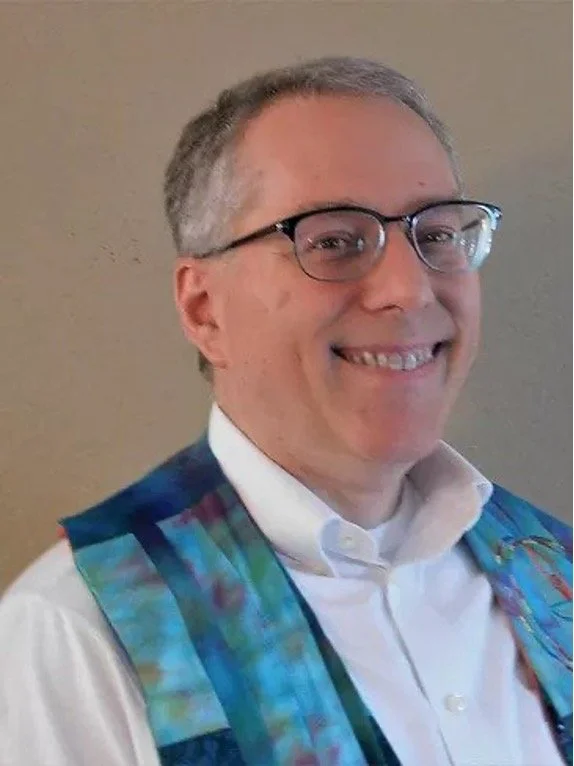 Rev. Rob Moore: A man with gray hair and glasses smiling, wearing a dress shirt and a colorful ministerial stole.