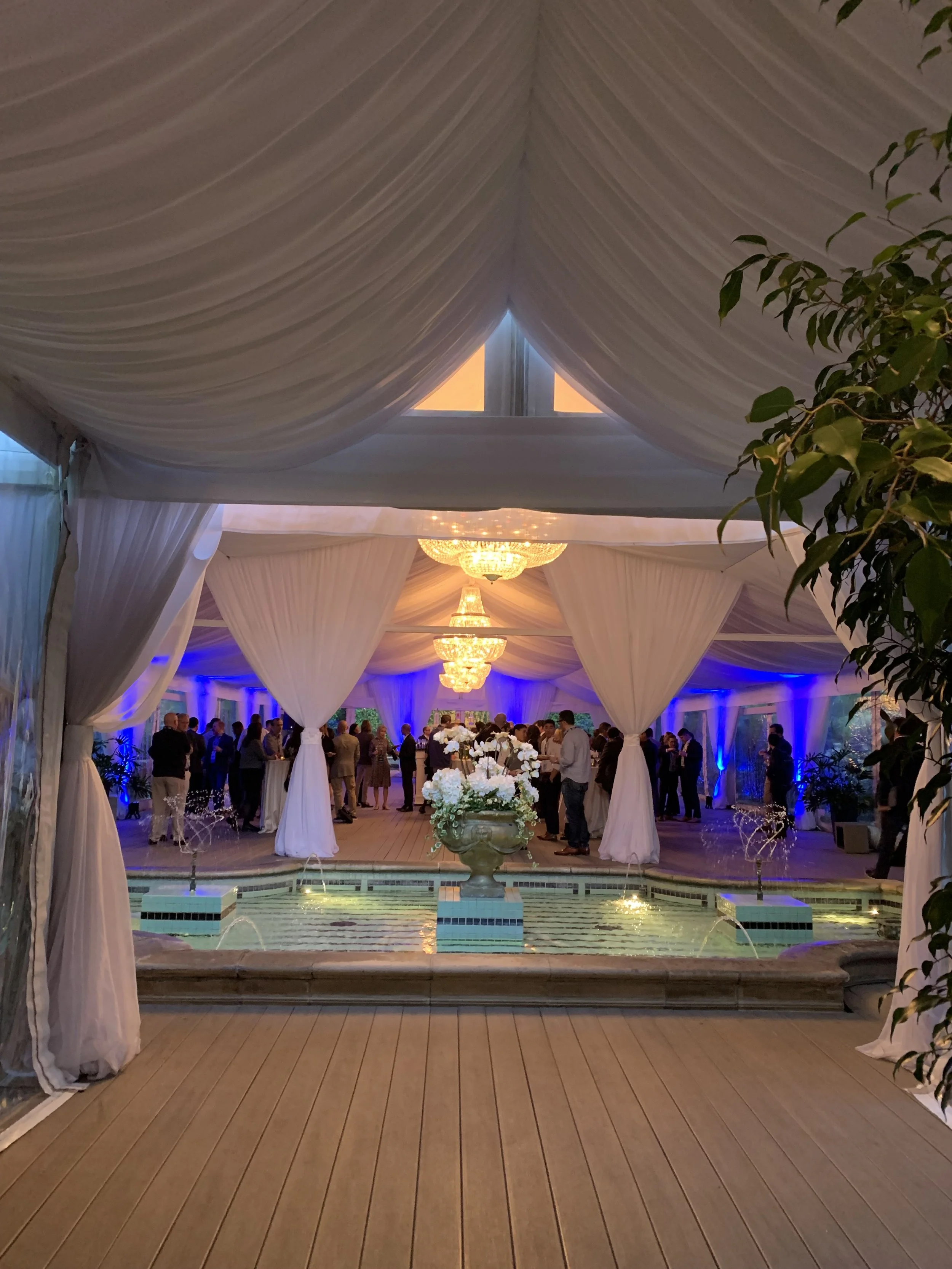 Elegant wedding reception tent with white draping, chandeliers, and floral decor