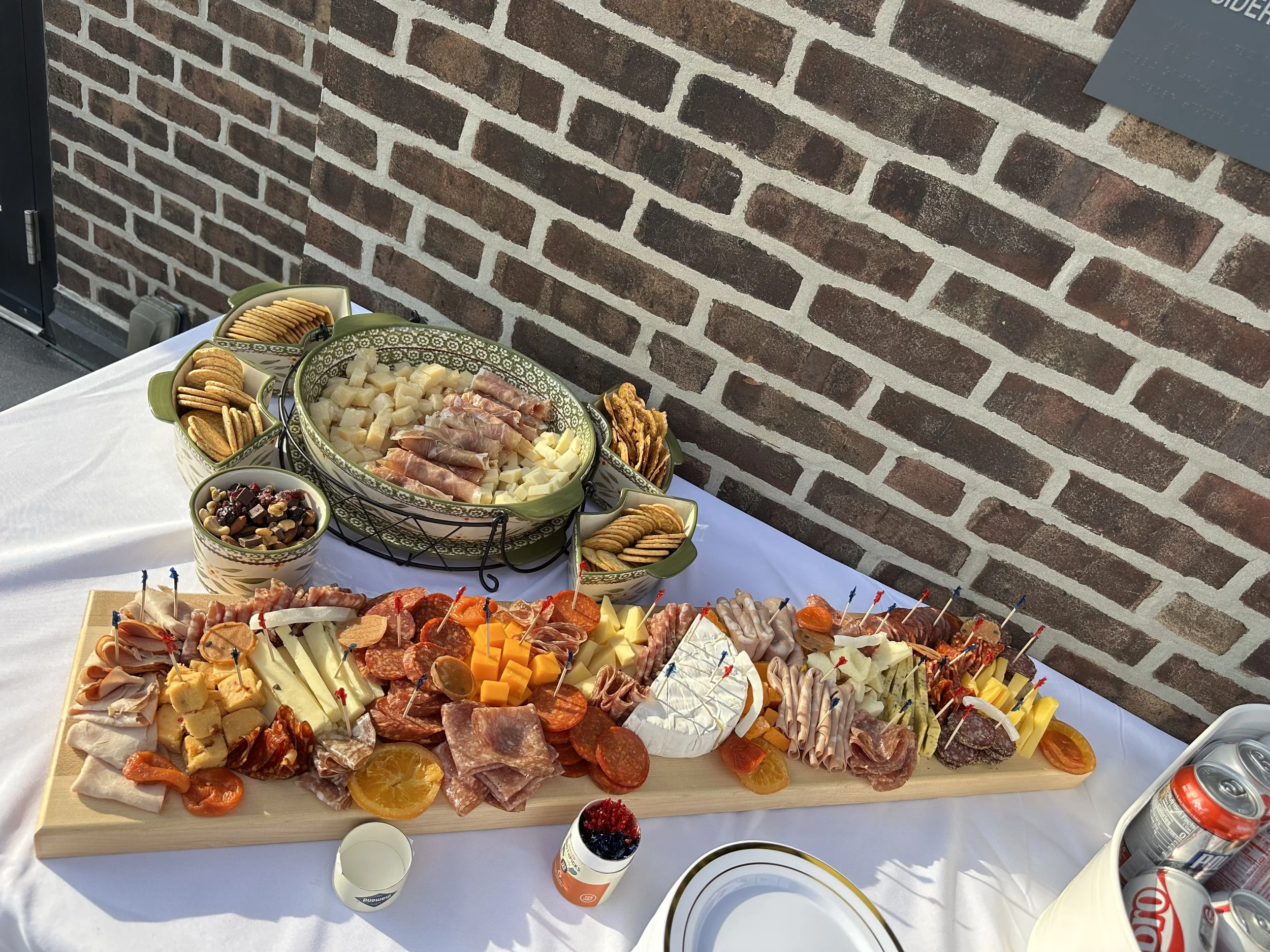 A charcuterie board with cheeses, meats, dried fruits, and nuts on a table outside against a brick wall.
