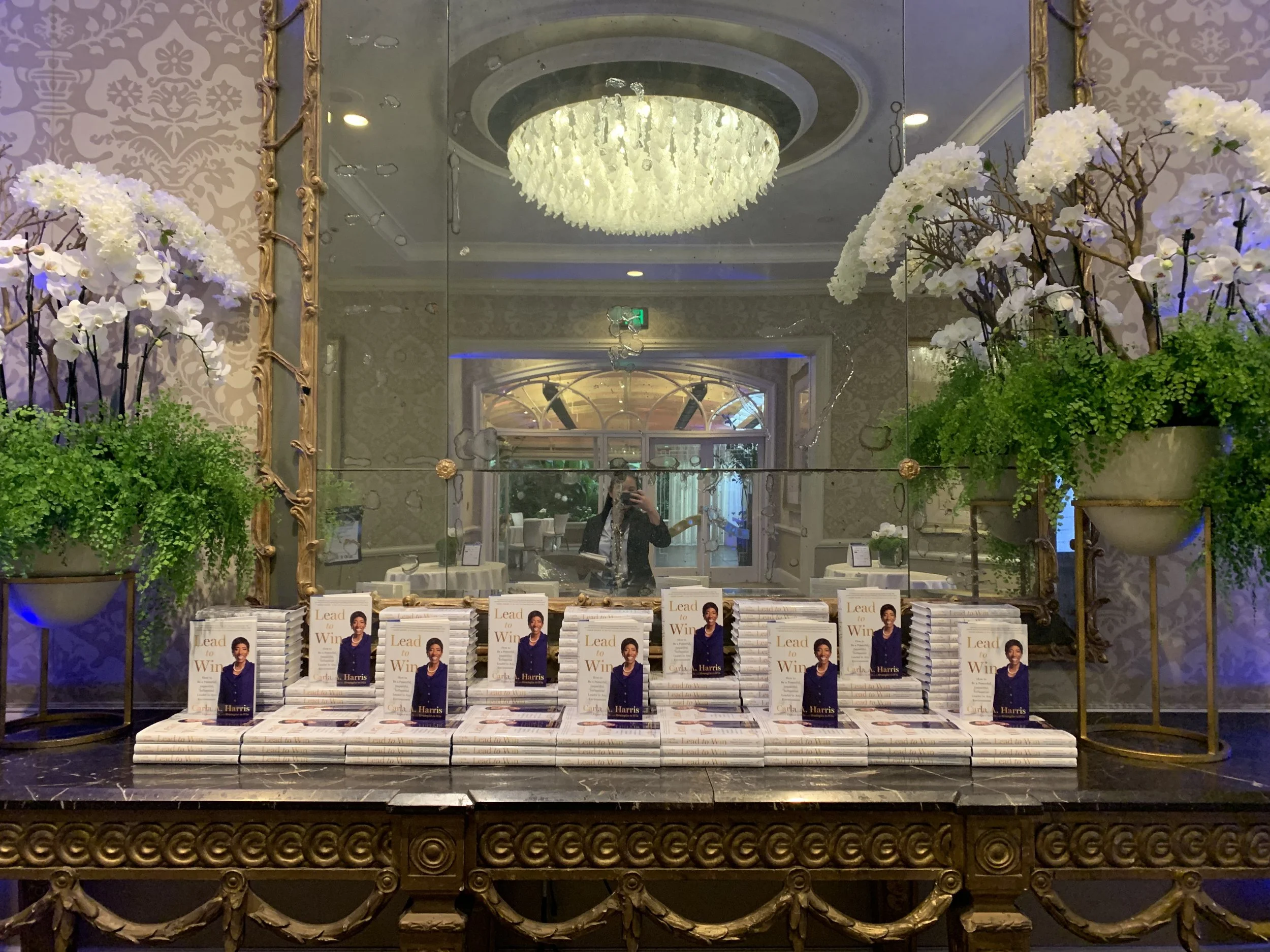 Lead to Win book display by Carla A. Harris at a corporate conference set with floral arrangements and chandelier