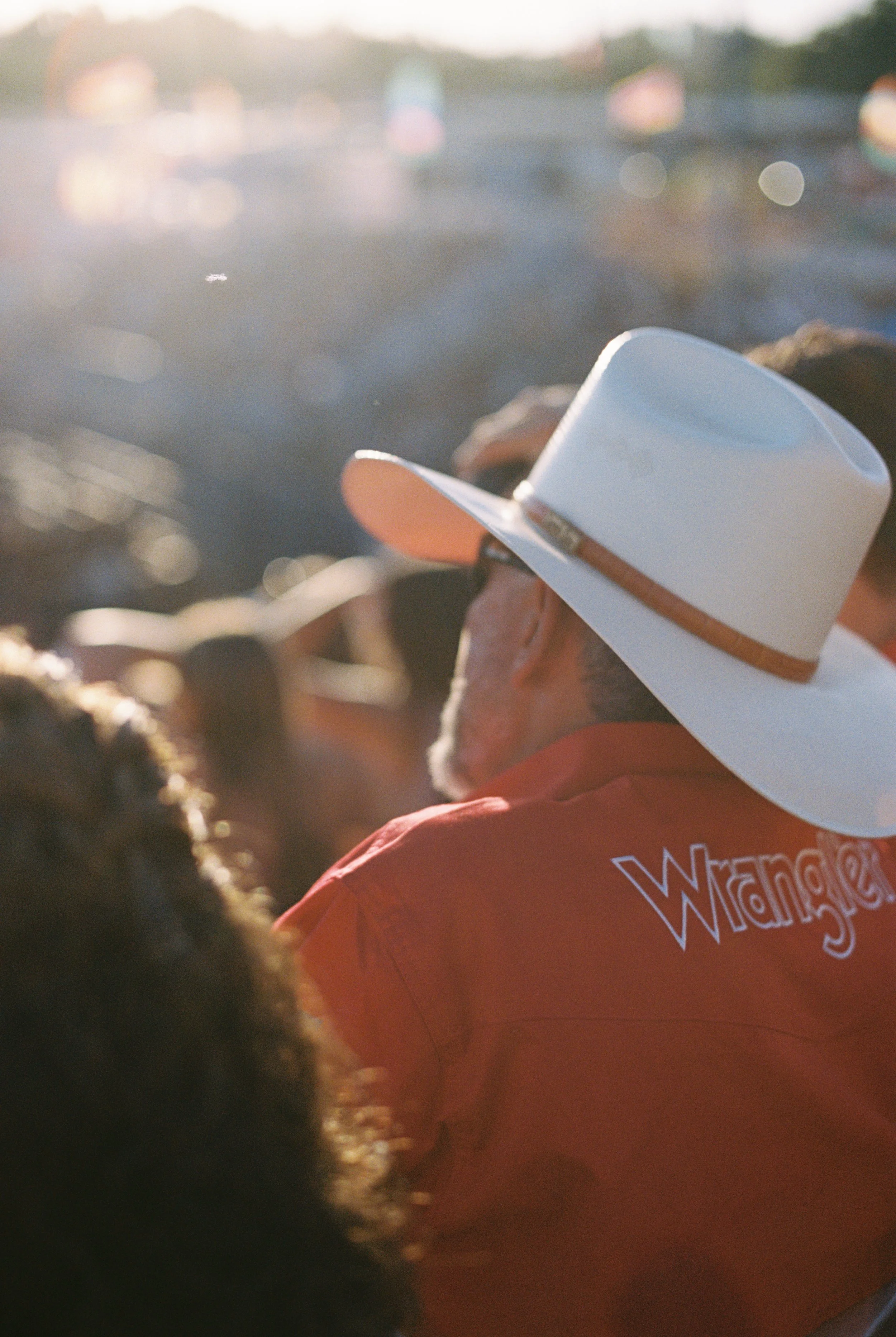 Person wearing a white cowboy hat and red jacket at an outdoor event during golden hour.