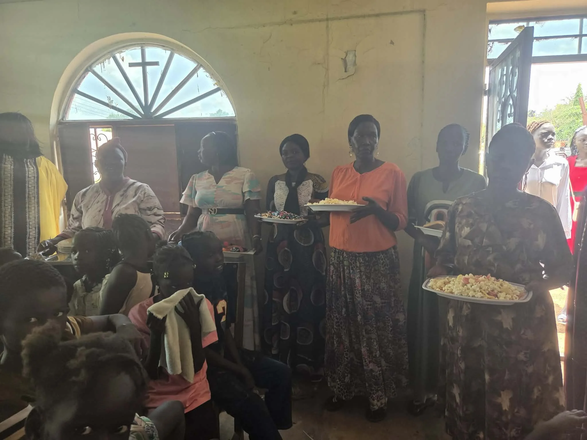 Group of women standing inside a church, with some holding trays of food for a gathering or celebration.