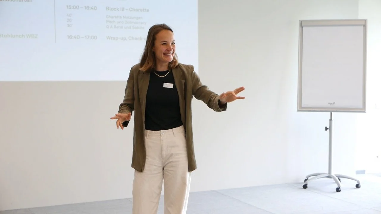 Eine Frau steht vor einer weißen Tafel in einem Konferenzraum, lächelnd und gestikulierend bei einer Präsentation.