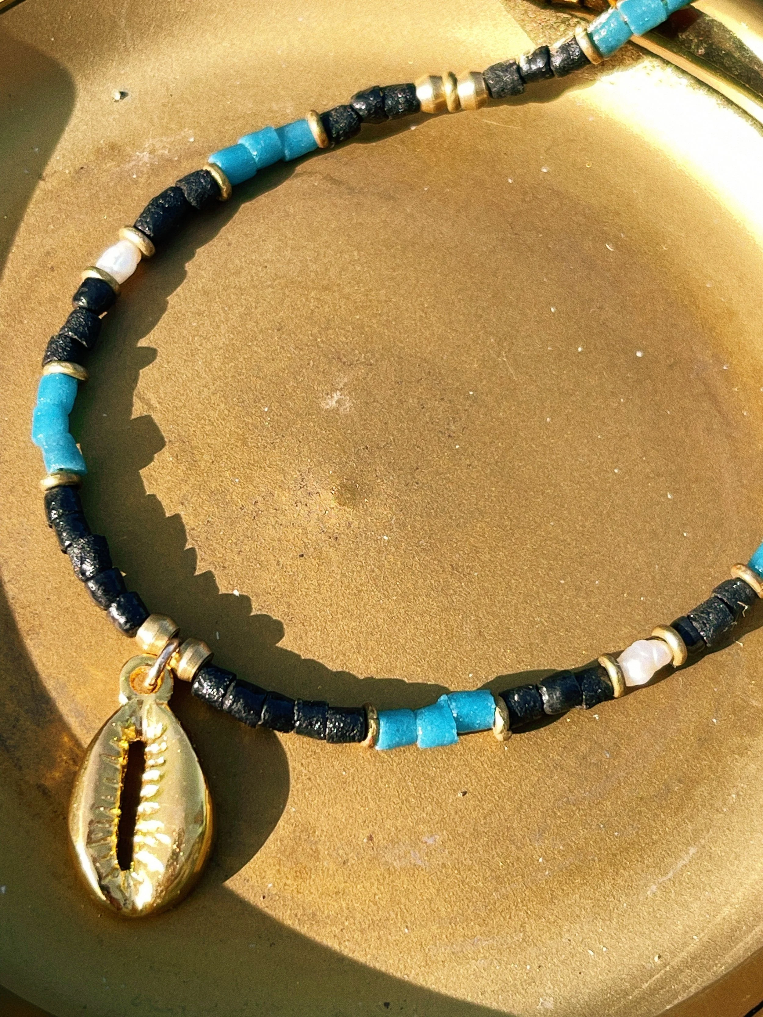 Close-up of the Attunement necklace by Tempered Earth, featuring turquoise, black, white, and brass beads with a cowrie shell pendant.
