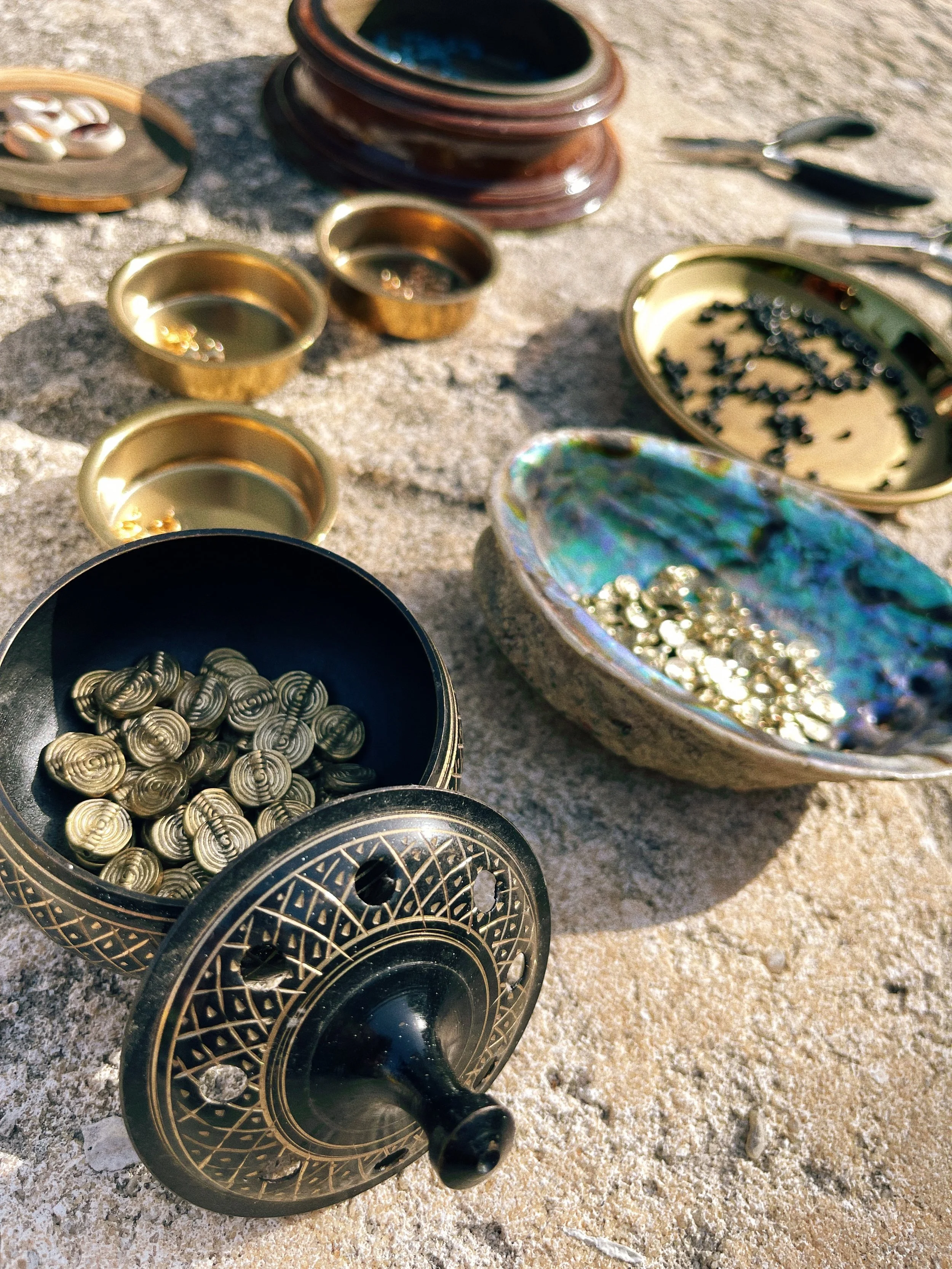 Beads, brass jewelry components, shells, tools, and small vessels arranged outdoors for jewelry making.