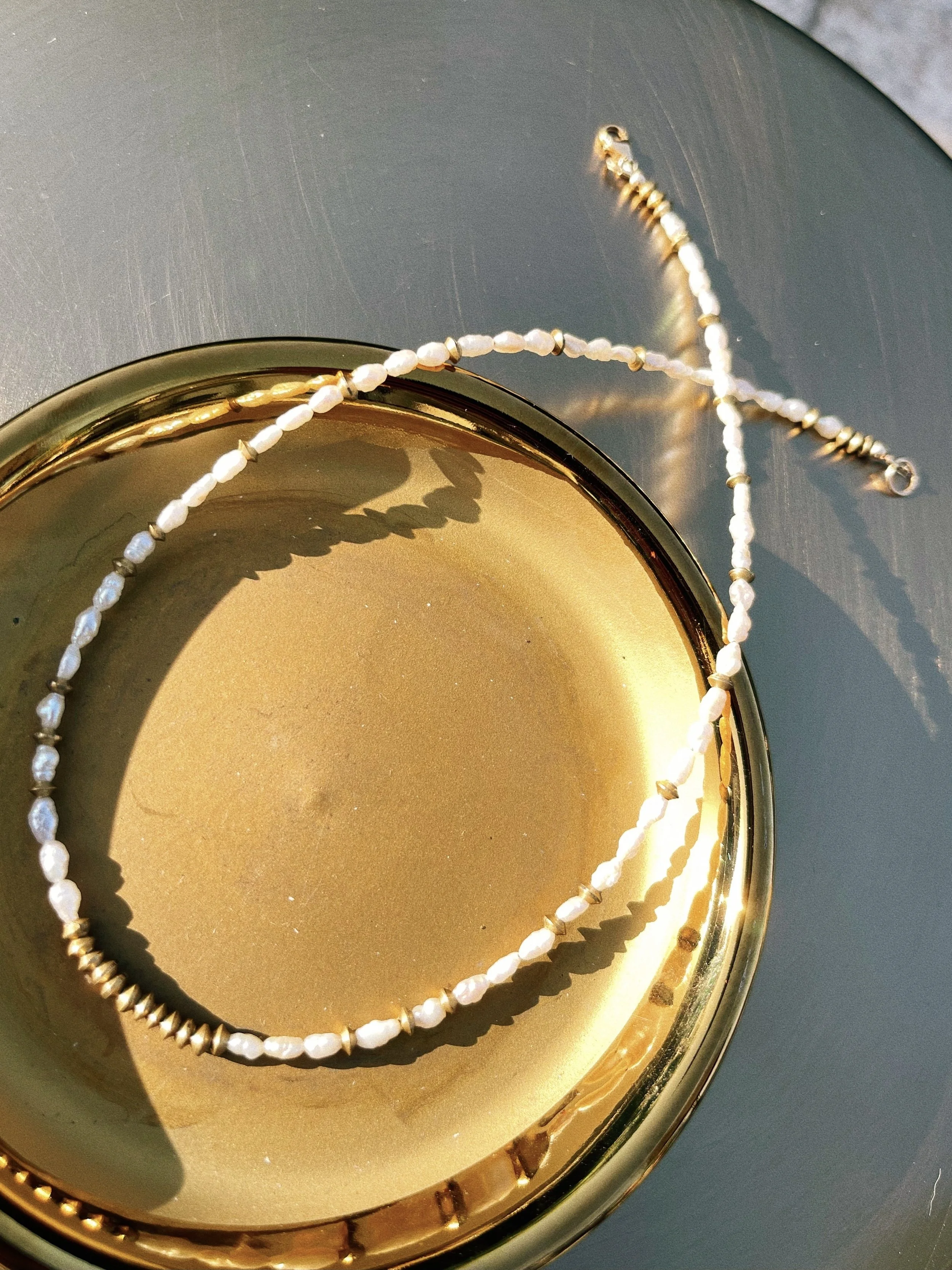 Moontide handmade beaded necklace by Tempered Earth, featuring baroque freshwater pearls and brass accents in a gold dish.