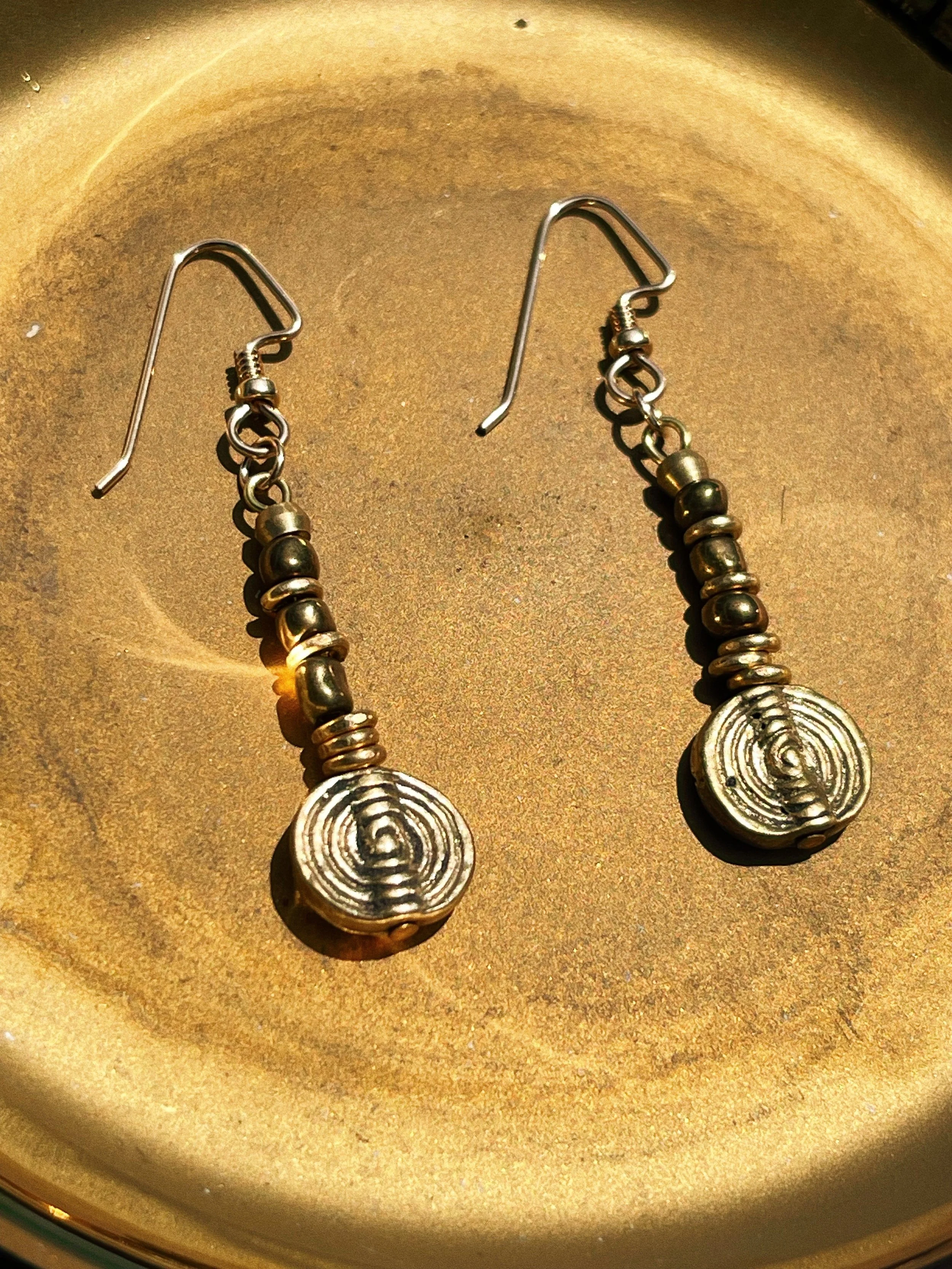 Solara handmade earrings by Tempered Earth, featuring circular brass pendants, photographed in a gold dish.