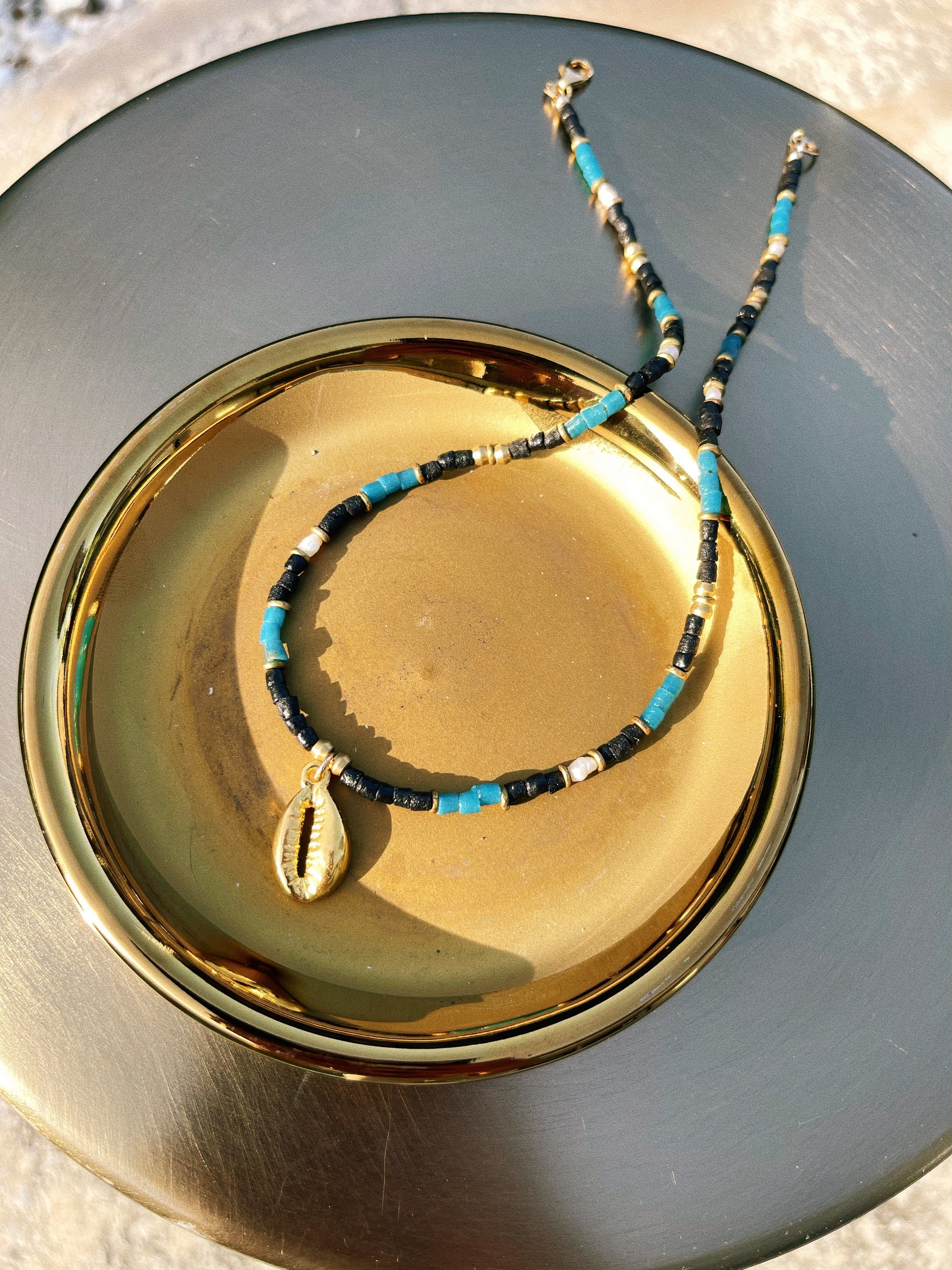 Attunement handmade beaded necklace by Tempered Earth, featuring turquoise, black, white, and brass beads with a cowrie shell pendant.