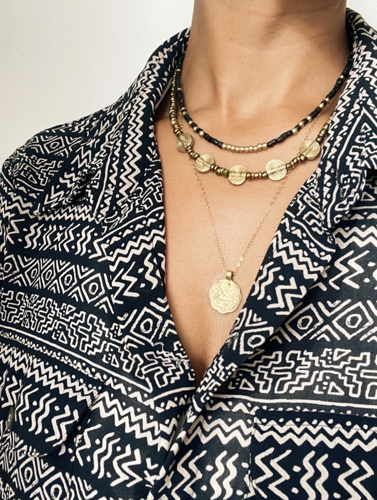 Layered handmade Tempered Earth necklaces worn together with a patterned black and beige shirt.
