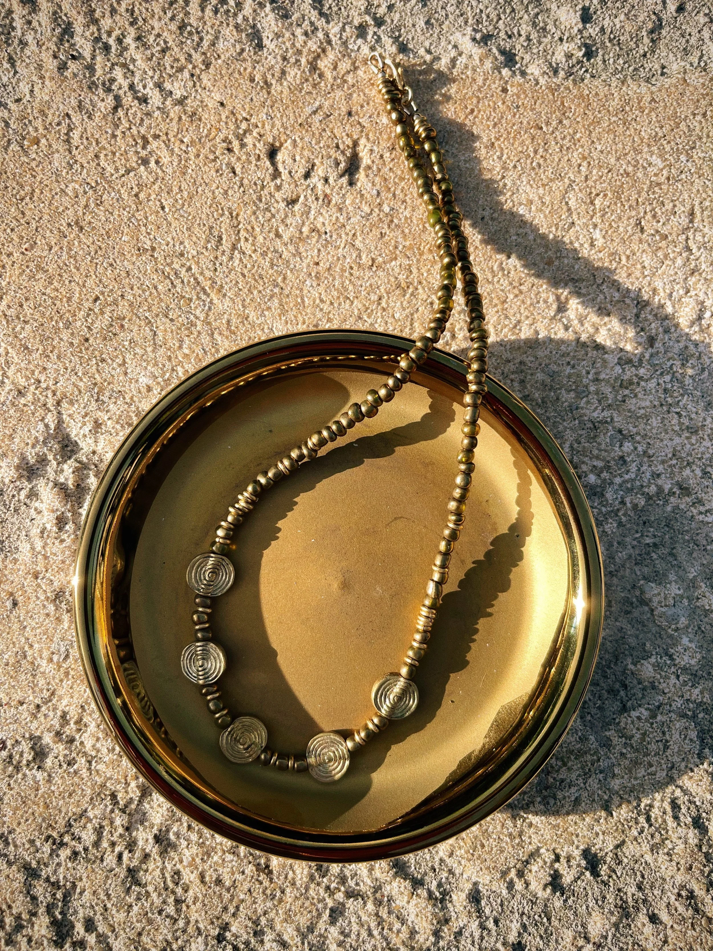 Radiance handmade beaded necklace by Tempered Earth, featuring circular brass elements, photographed in a gold dish.
