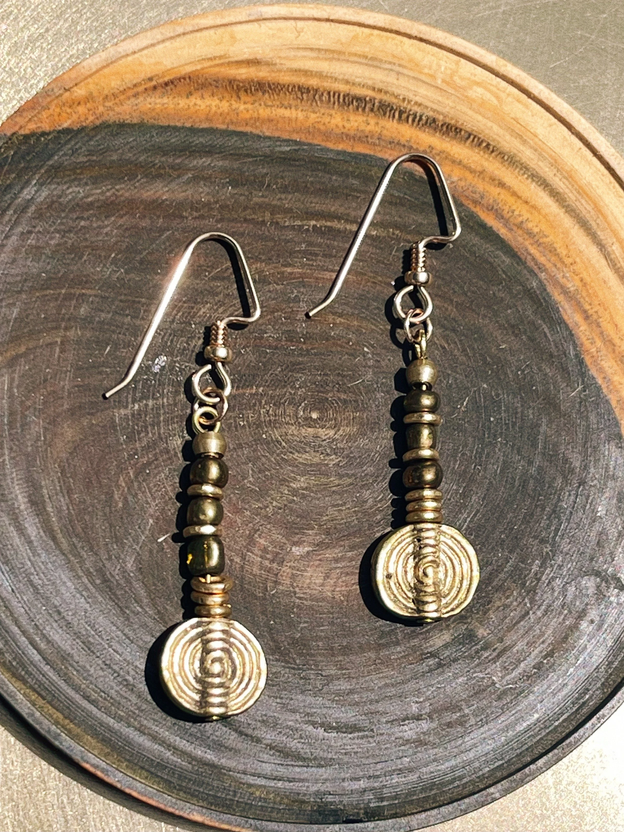 Solara handmade earrings by Tempered Earth, featuring circular brass pendants, photographed on a wooden surface.
