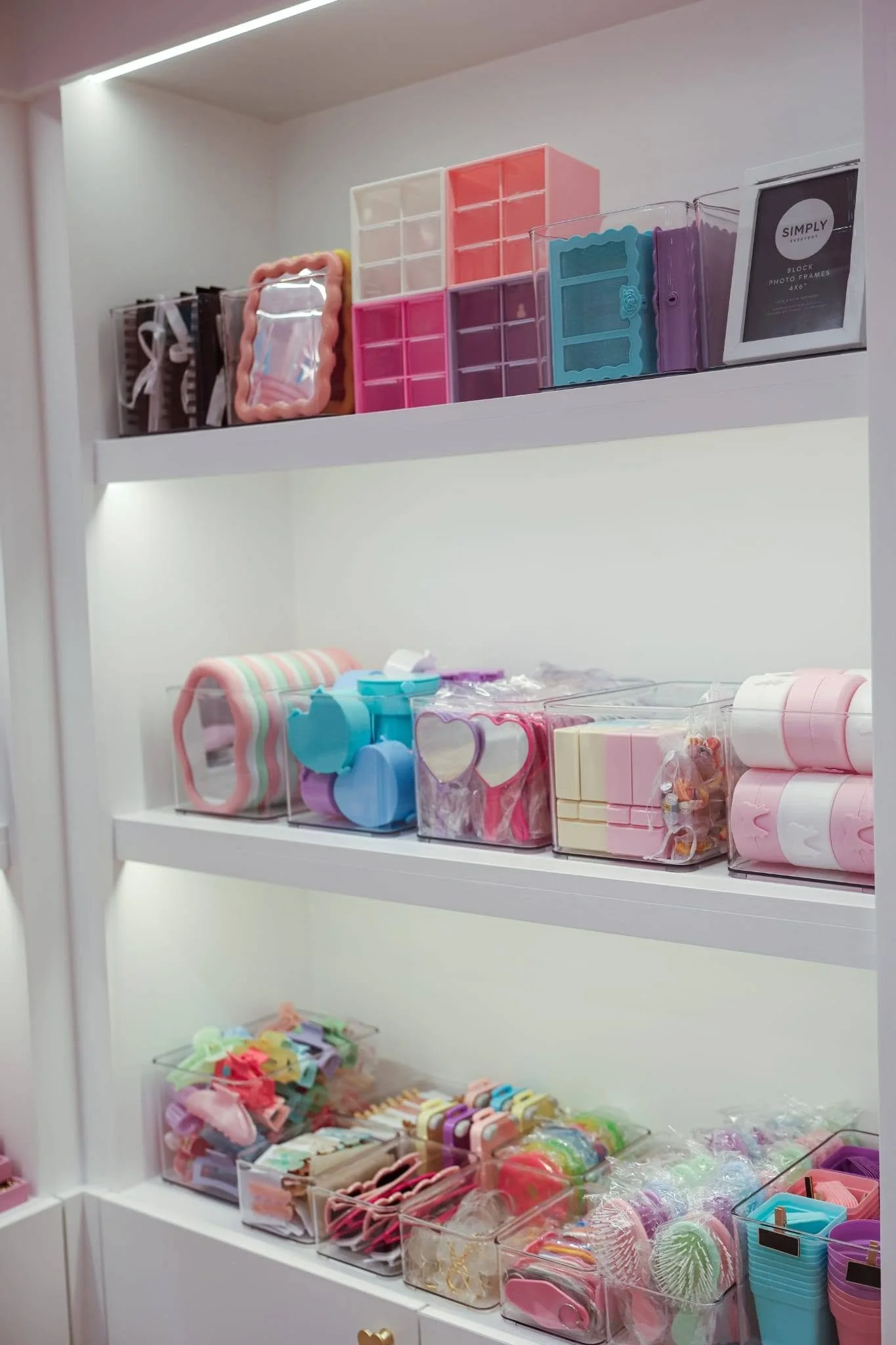 White shelves filled with pastel-colored organizing containers and accessories including hairbands, hair clips, scrunchies, and small storage boxes.