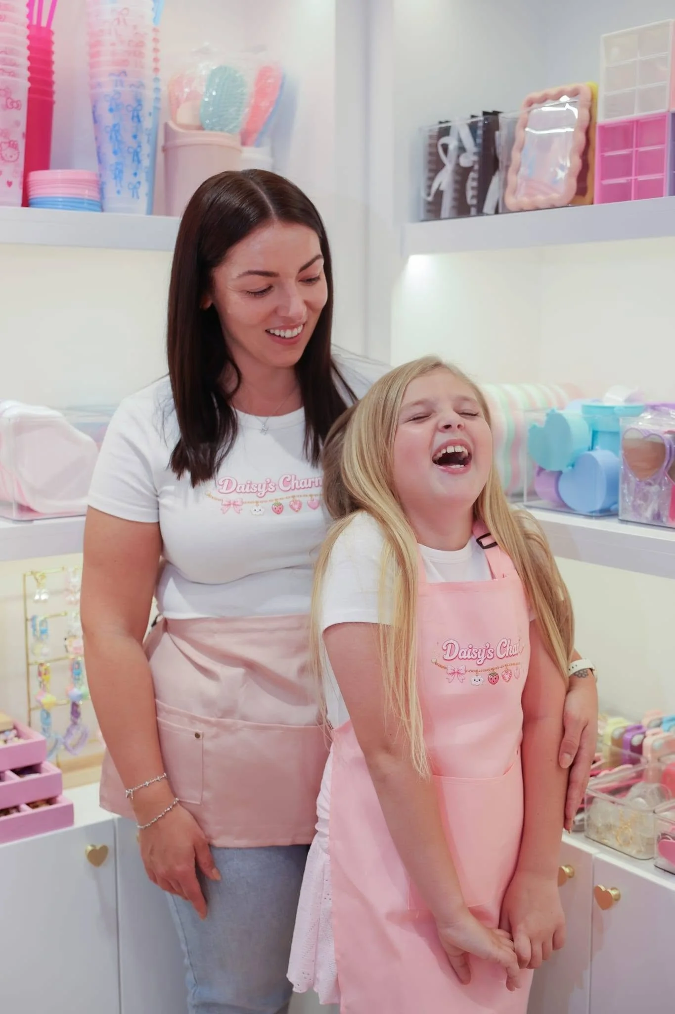 A woman and a young girl smiling in a brightly lit store, surrounded by pastel-colored accessories and decorations.