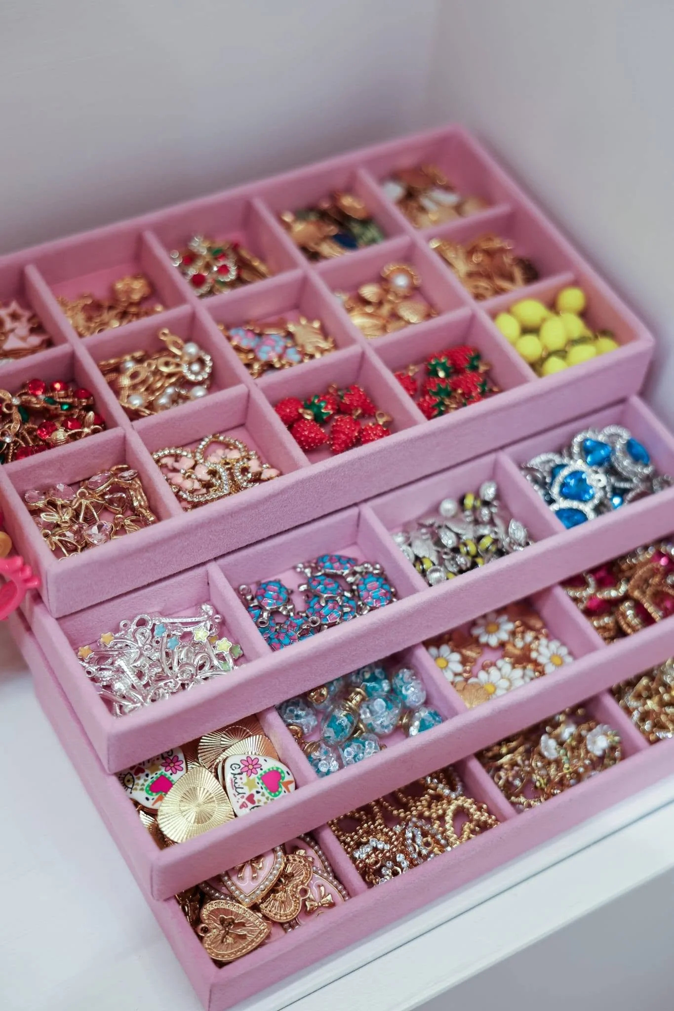 A pink jewelry organizer box filled with various colorful earrings, rings, and decorative pins.