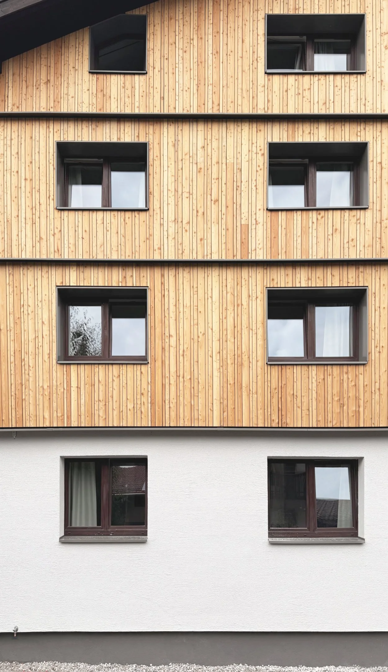Holzfassade und dunkelgrauen Fensterlaibungen und Putz mit Besenstrichoptik im Mitarbeiterhaus J in Mittenwald, geplant von d'ns Studio