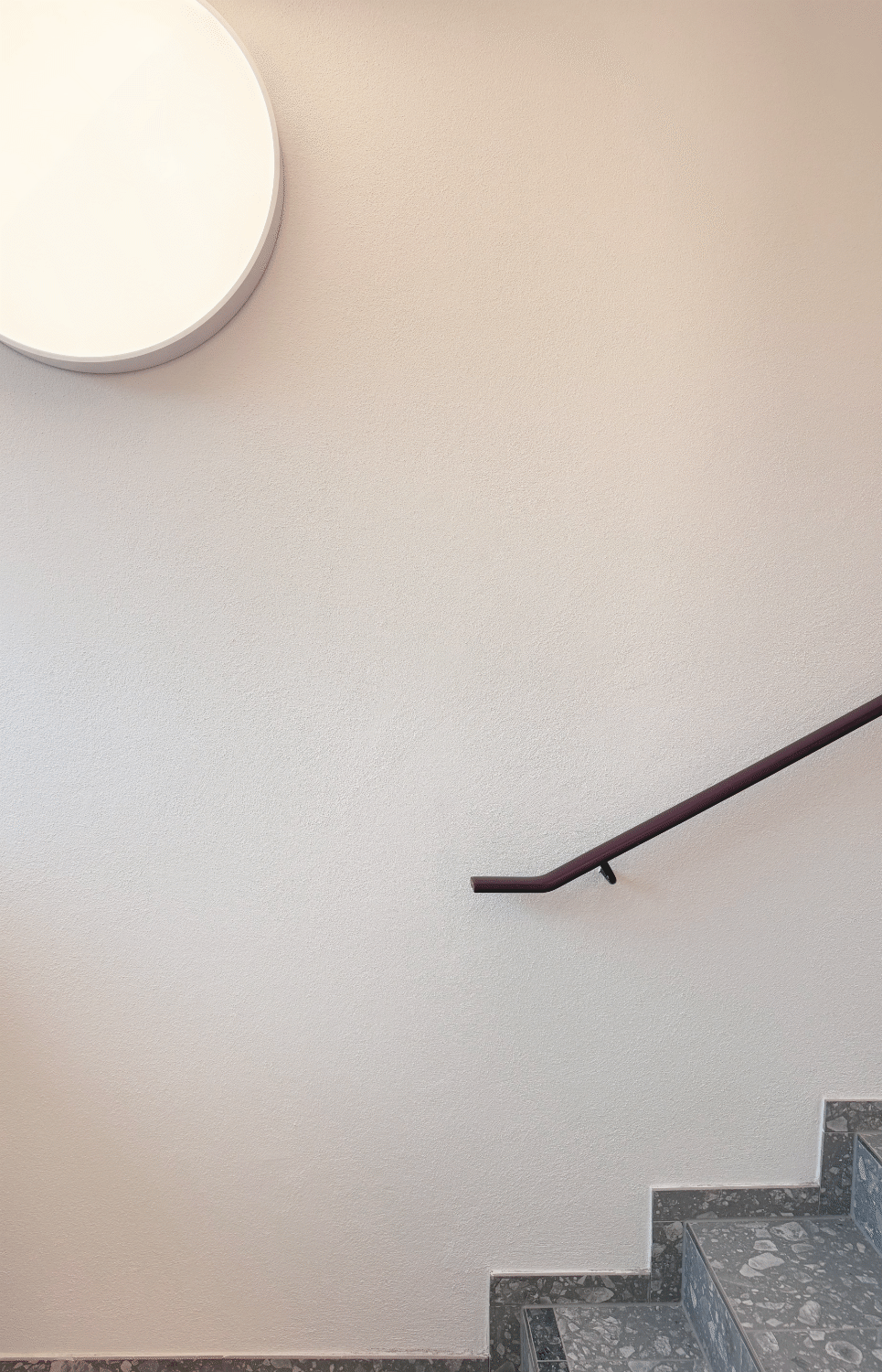 Treppenhaus mit Wandleuchte und dunkelrotem Handlauf im Mitarbeiterhaus J in Mittenwald, geplant von d'ns Studio