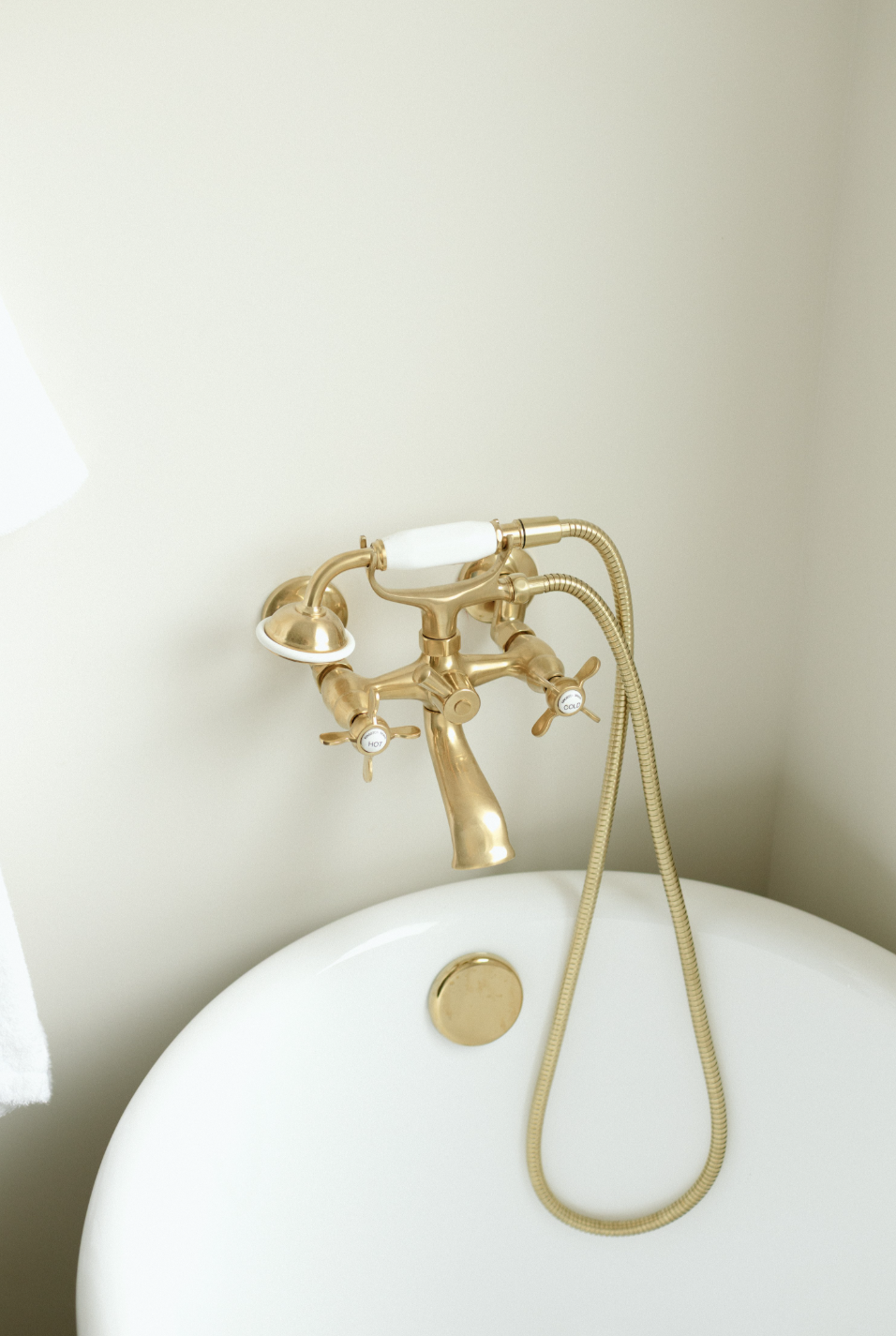 Close-up of a vintage-style, gold bathtub faucet with a hand-held shower head and vintage handles, mounted above a white bathtub.