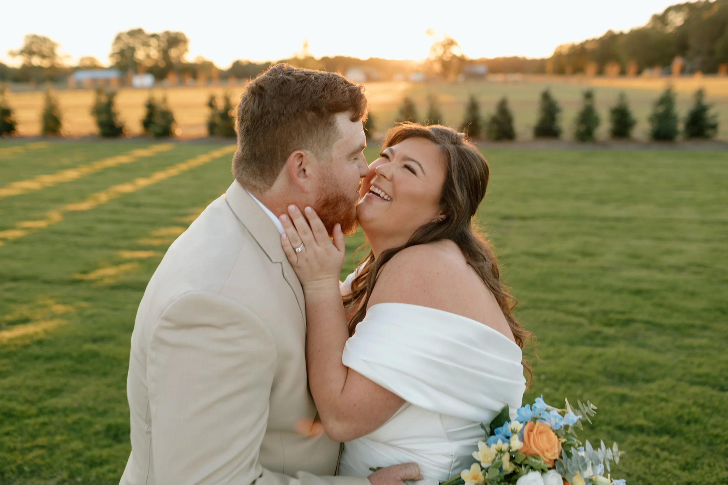 A couple in wedding attire sharing a joyful moment outdoors at sunset.