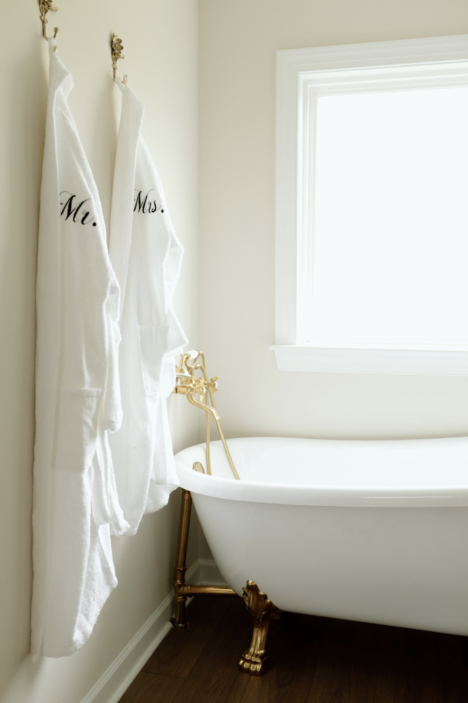 Bathroom with a white clawfoot bathtub and two plush bathrobes labeled 'Mr.' and 'Mrs.' hanging on hooks.
