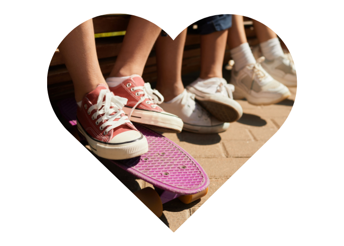 Close-up of children's feet sitting on skateboards, with red and white sneakers, on a brick patio, framed inside a heart-shaped cutout.