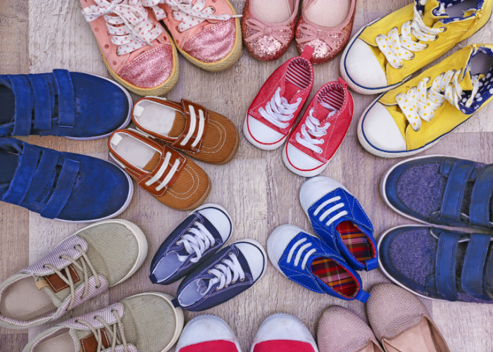 Various colorful children's shoes arranged in a circle on a wooden floor.