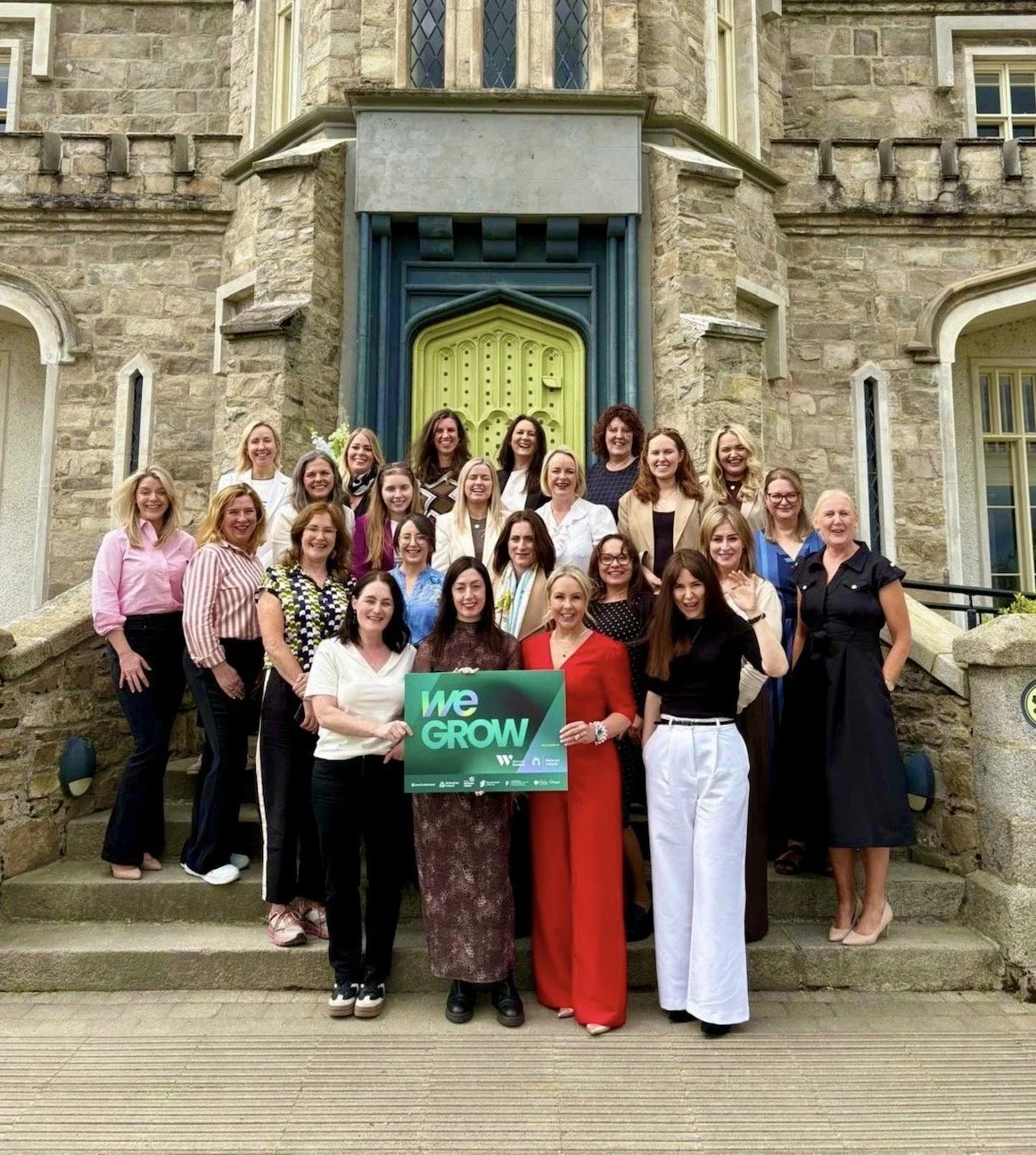 Group of women standing on the steps of a stone building, holding a sign that reads "We Grow".