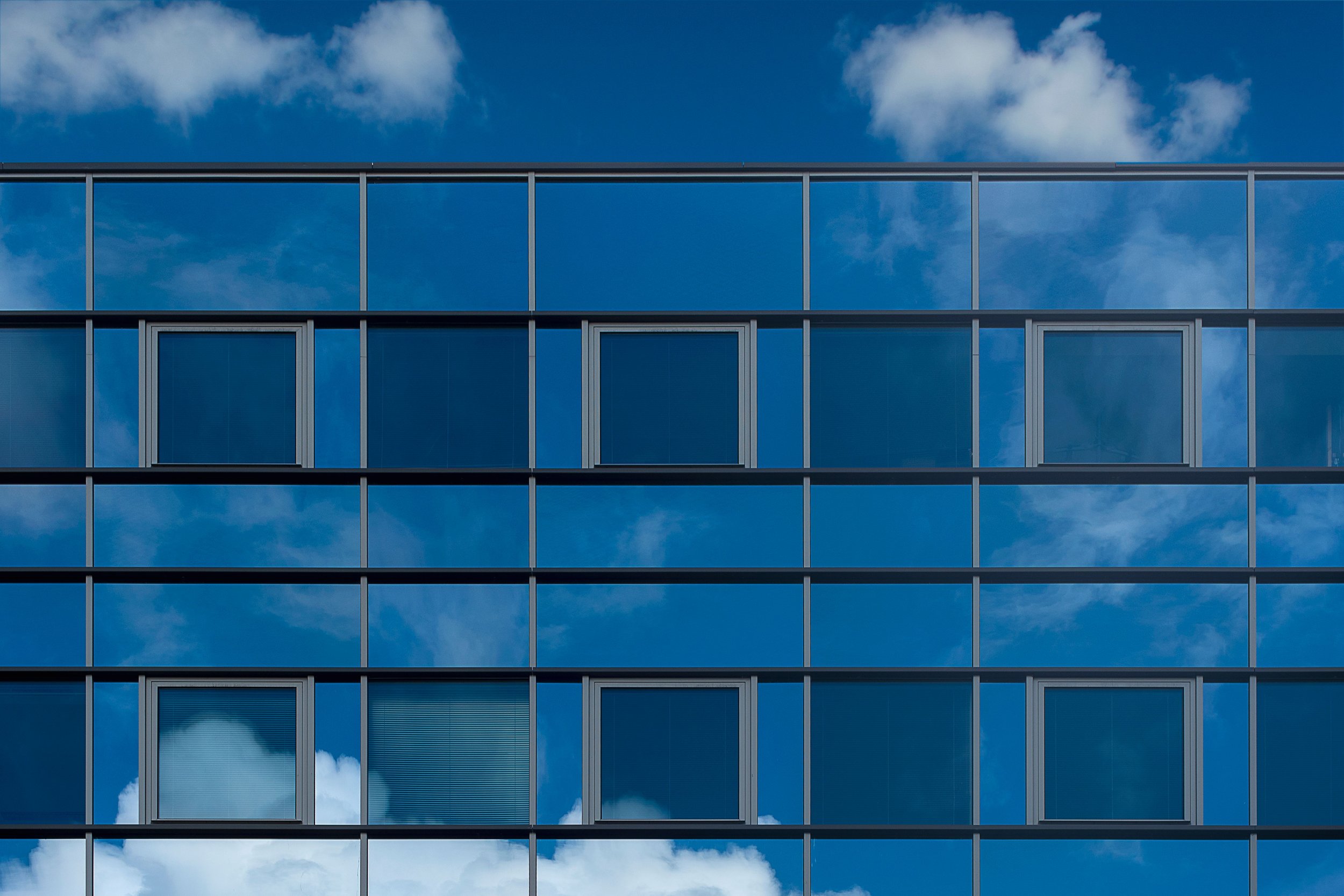 The image shows a modern glass building with blue-tinted windows reflecting the sky and clouds.