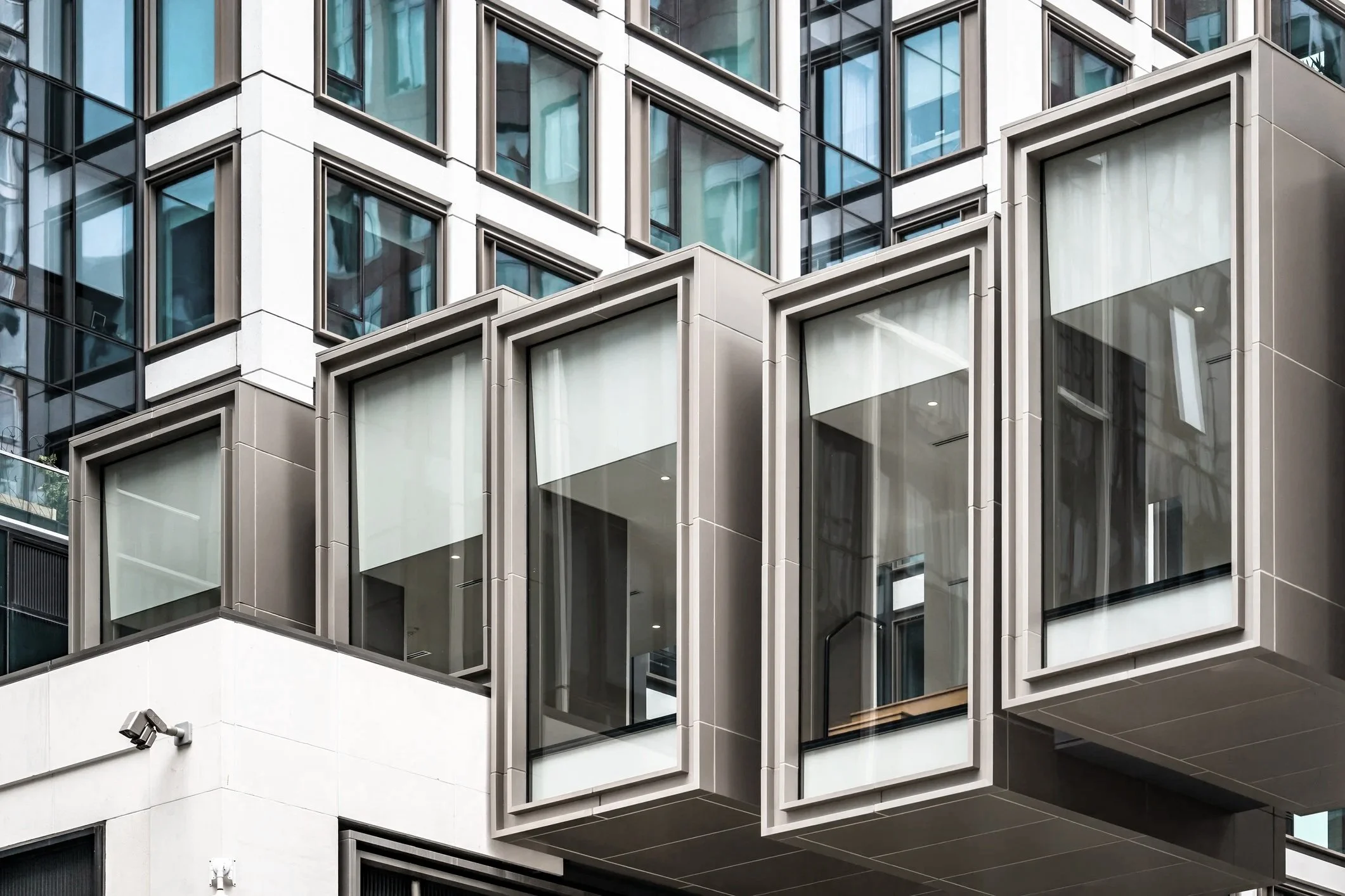 Close-up view of a modern multi-story building facade with large glass windows and protruding architectural elements in gray and white tones.