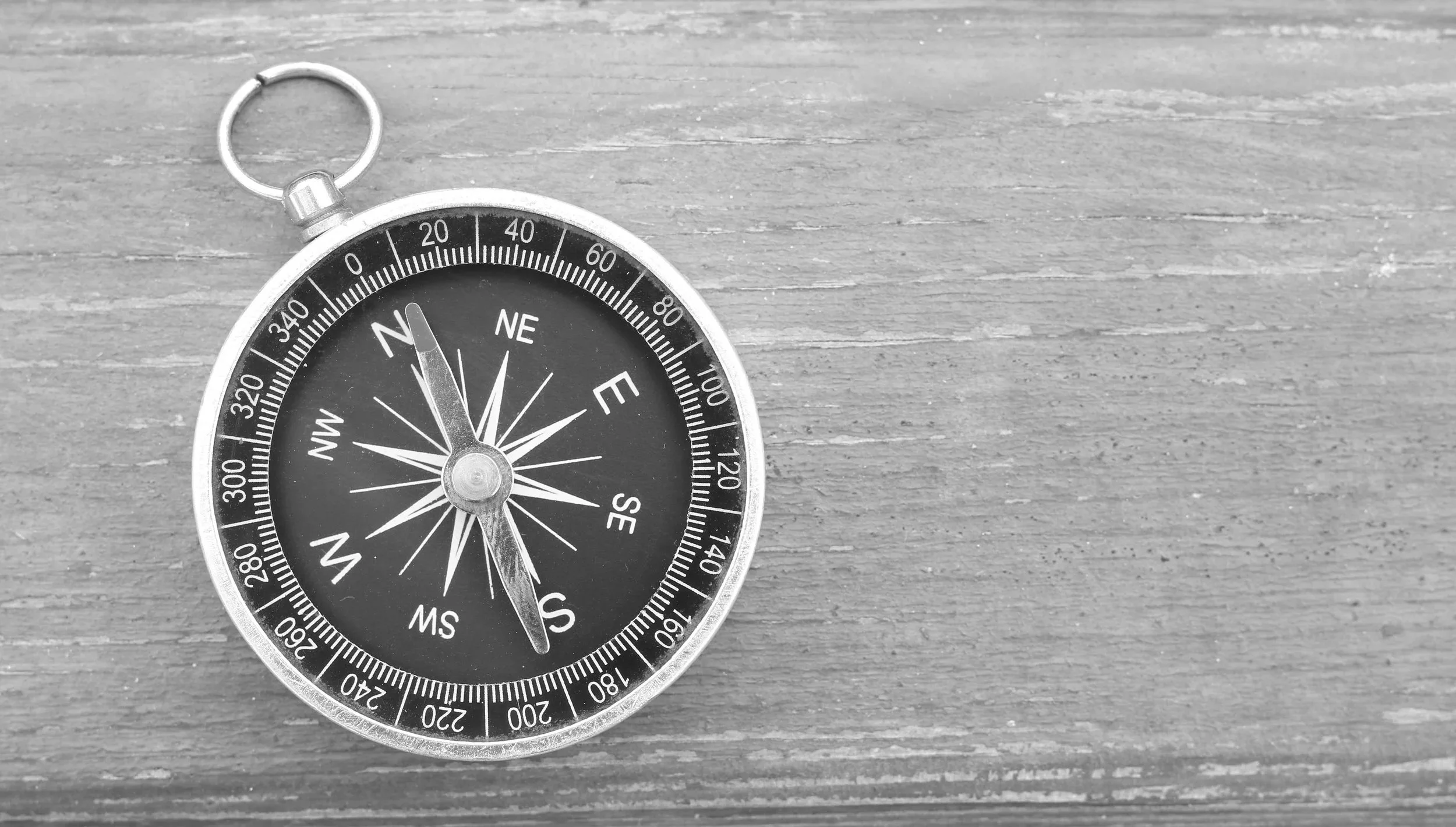 Black and white photograph of a pocket compass resting on a wooden surface.